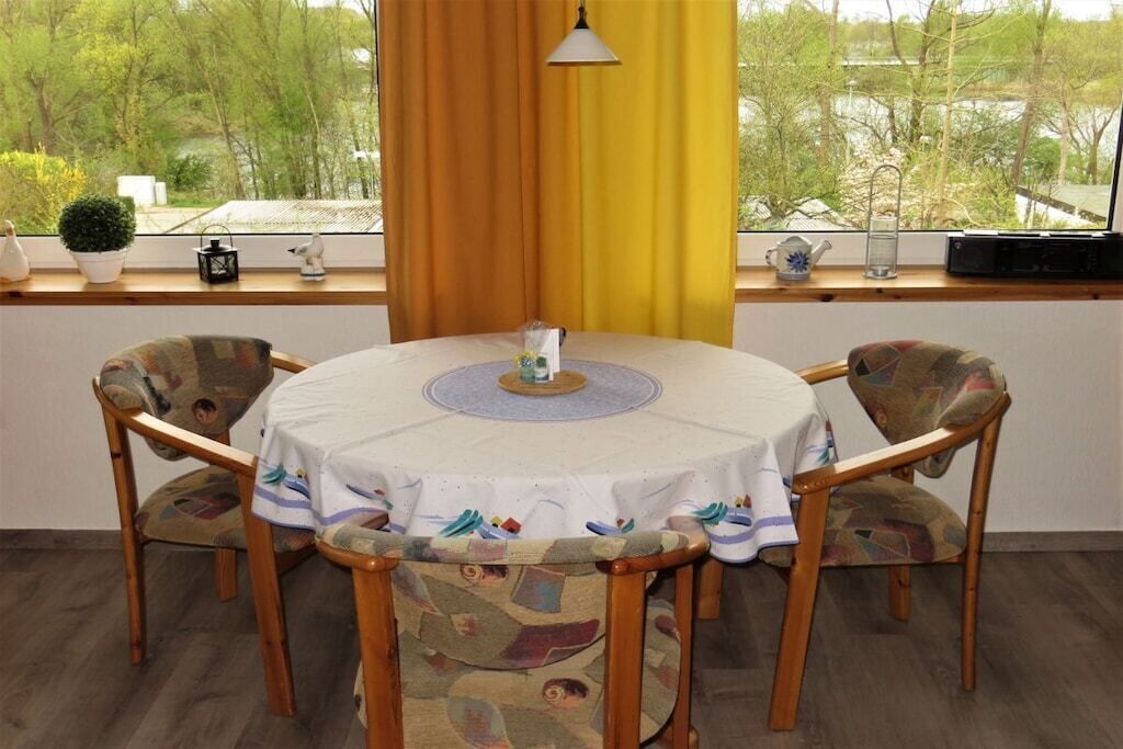 Una mesa redonda con mantel blanco, rodeada por cuatro sillas estampadas, frente a una ventana con cortinas.