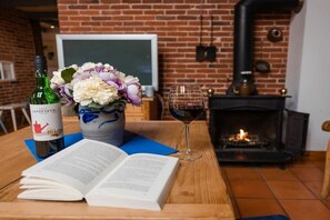 A cozy room with a fireplace, a book, a bottle of wine, and a vase of flowers on a wooden table. - Holiday home with 2 bedrooms (Südbrookmerland)