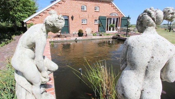Un bâtiment en briques avec un étang, deux statues en pierre et une pelouse.