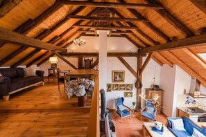 A spacious loft with a high ceiling, wooden beams, a fireplace, a sofa, a dining table, and a chandelier. - Holiday home with 2 bedrooms (Südbrookmerland)