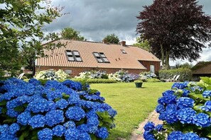 Ein Haus mit einem Ziegeldach, umgeben von einem gepflegten Rasen und verschiedenen blühenden Pflanzen.