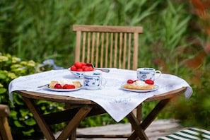 Una mesa con mantel blanco, una silla de madera y un cuenco de fresas.