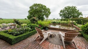 Une terrasse de jardin avec un sol en briques, deux fauteuils Adirondack en bois, une petite table ronde et un bassin orné de nénuphars.