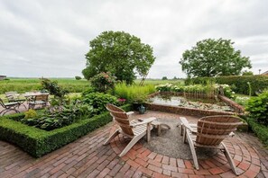 Un patio jardín con suelo de ladrillo, dos sillas Adirondack de madera, una mesita redonda y un estanque con nenúfares.