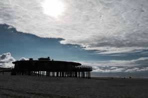 Eine Stegkonstruktion mit einem kreisförmigen Gebäude, das sich über einen Sandstrand erstreckt.