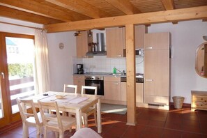 A kitchen with wooden cabinets, a dining table with chairs, and a view through an open door. - "West" in the holiday home "Keilbergblick" (Kurort Oberwiesenthal)