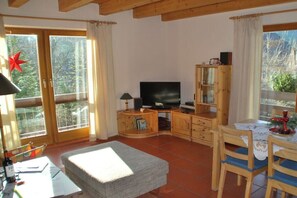 A cozy living room with a television, wooden cabinets, a dining table with chairs, and large windows with curtains. - "West" in the holiday home "Keilbergblick" (Kurort Oberwiesenthal)