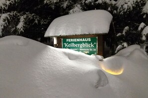 Een met sneeuw bedekte bord met 'FERIENHAUS Keilbergblick', met een gedeeltelijk zichtbaar gebouw erachter.