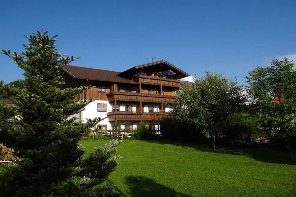 A multi-story wooden building with balconies, surrounded by a well-maintained lawn and trees.