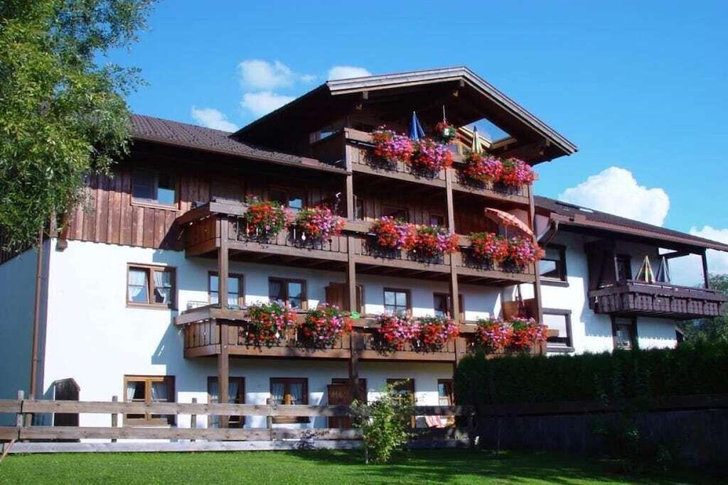 A multi-story building with balconies adorned with flowers, a wooden facade, and a clear sky.