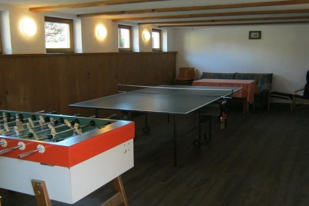 A room with a foosball table, a ping pong table, and a sofa.