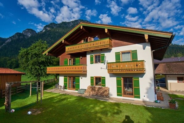 A two-story chalet with a balcony, a wooden deck, and a mountain backdrop. - Alpine view from the Thiele house (Schönau am Königssee)