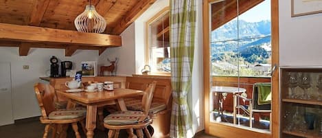 A wooden dining area with a table and chairs, a hanging light fixture, and a view of mountains through a window.