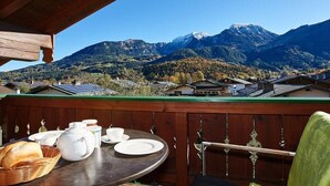 Een gedekte tafel met witte servies en brood, met uitzicht op een bergachtig landschap met huizen.