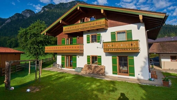 Een chalet met twee verdiepingen, een balkon, een houten terras en een berg op de achtergrond.