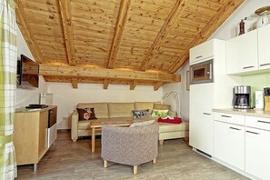Ein gemütlicher Wohnbereich mit Holzbalkendecke, einer Couch, einem kleinen Tisch und einer Küchenzeile mit einer Mikrowelle.