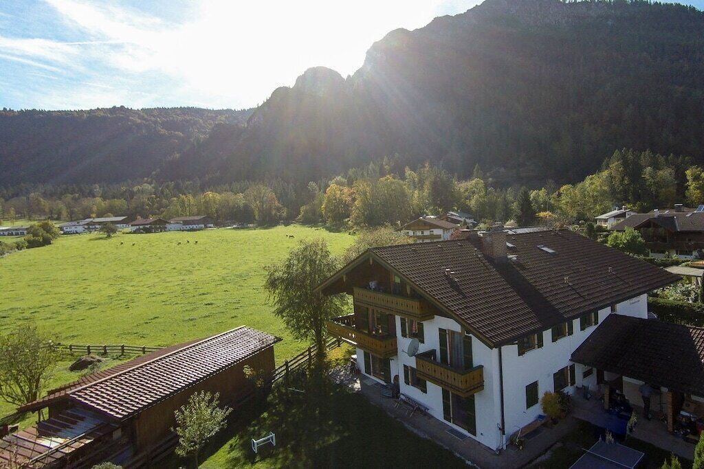 Ein zweigeschossiges Gebäude mit einem Balkon, umgeben von einem grünen Feld und Bergen im Hintergrund.
