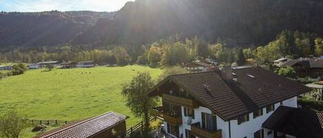 A two-story building with a balcony, surrounded by a green field and mountains in the background.