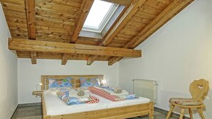 Een slaapkamer met een houten bed, dakraam, radiator en een houten stoel.