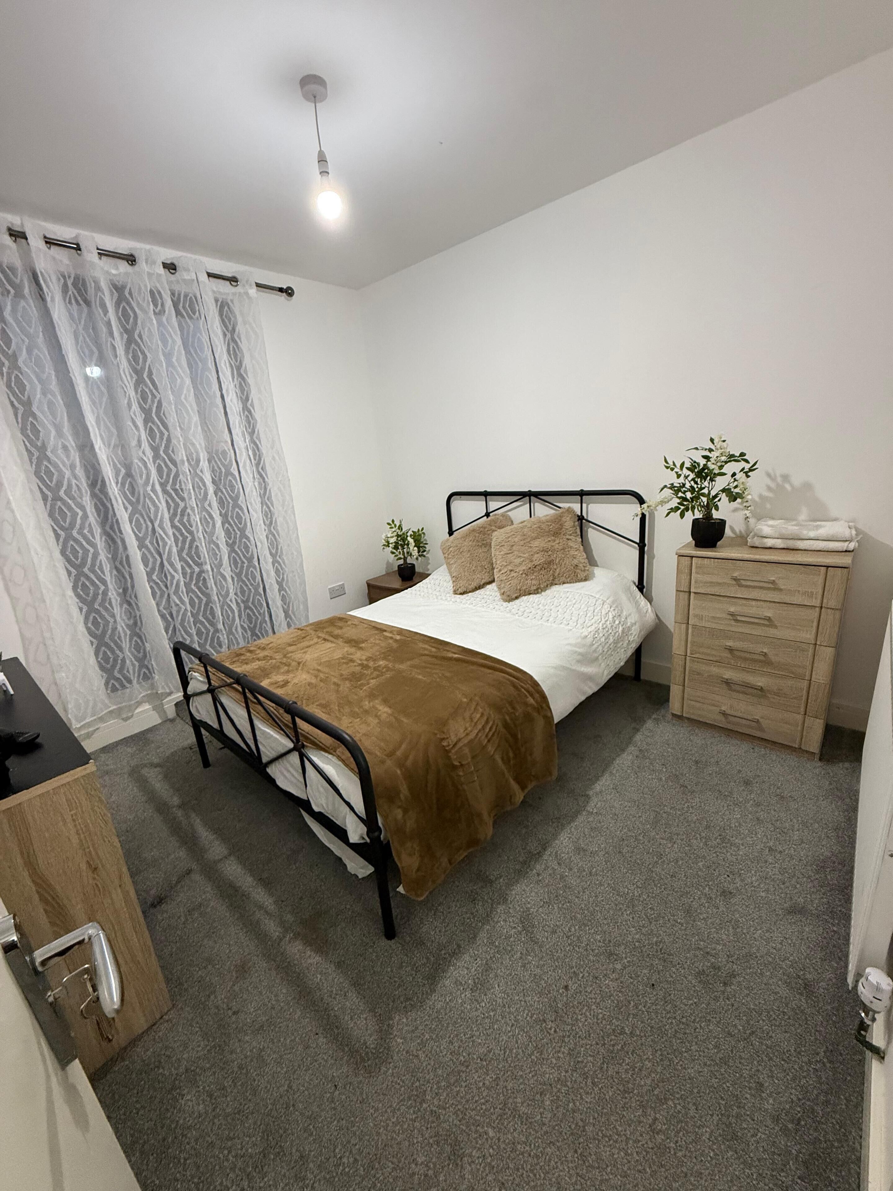Un dormitorio con una cama individual, un aparador de madera, una mesita de noche, una planta en maceta y una cortina.