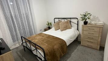 Un dormitorio con una cama individual, un aparador de madera, una mesita de noche, una planta en maceta y una cortina.