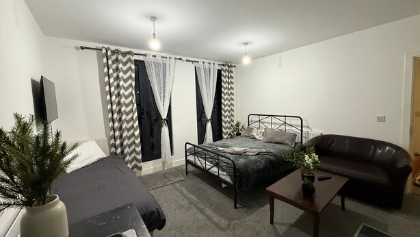 A bedroom with a bed, a bedside table, a chair, a TV, and a window with curtains.