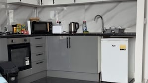 A compact kitchen with grey cabinets, a microwave, a kettle, and a small refrigerator.