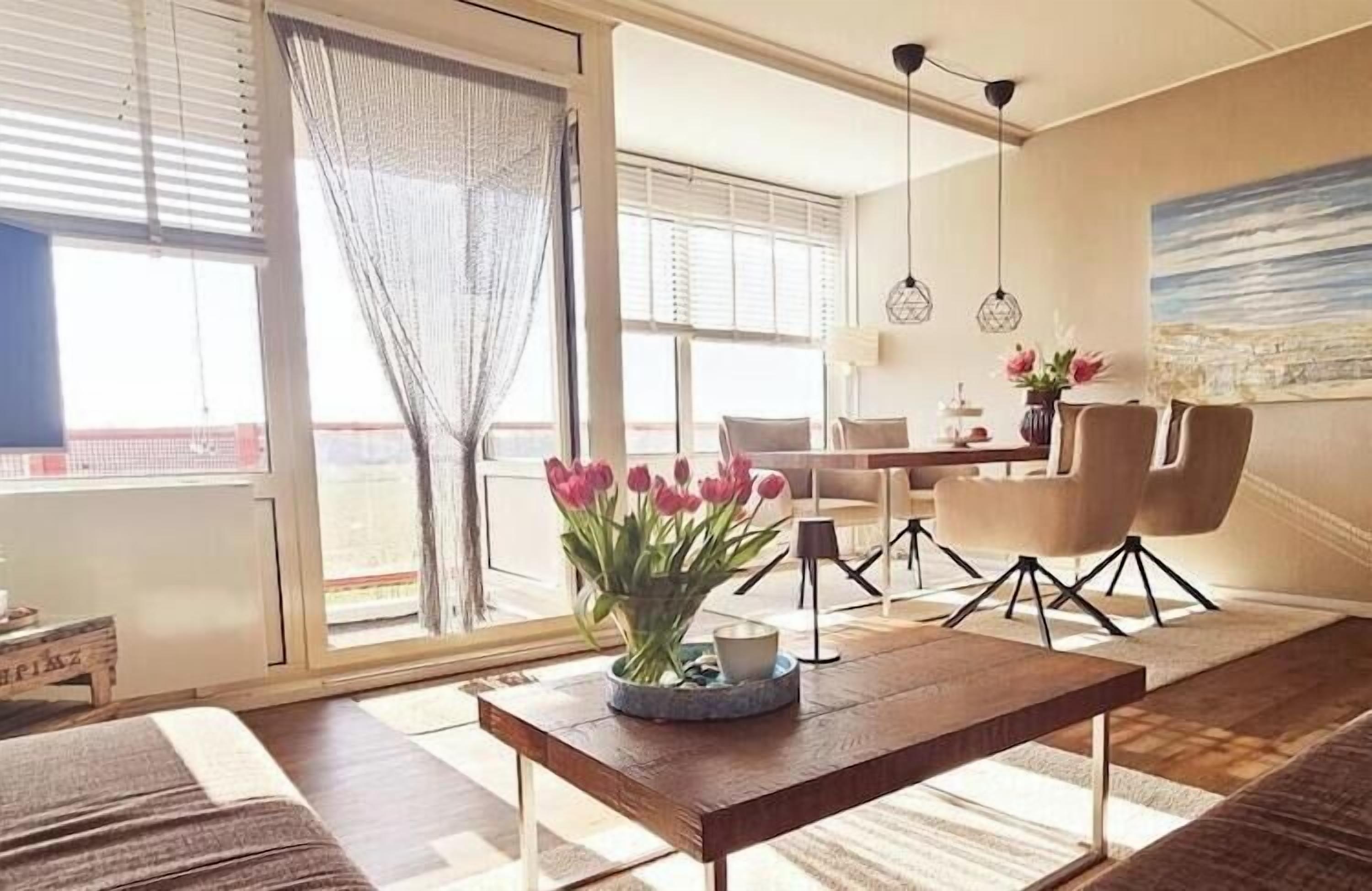 A modern living room with a wooden coffee table, a dining area with chairs, and a large window with a view.