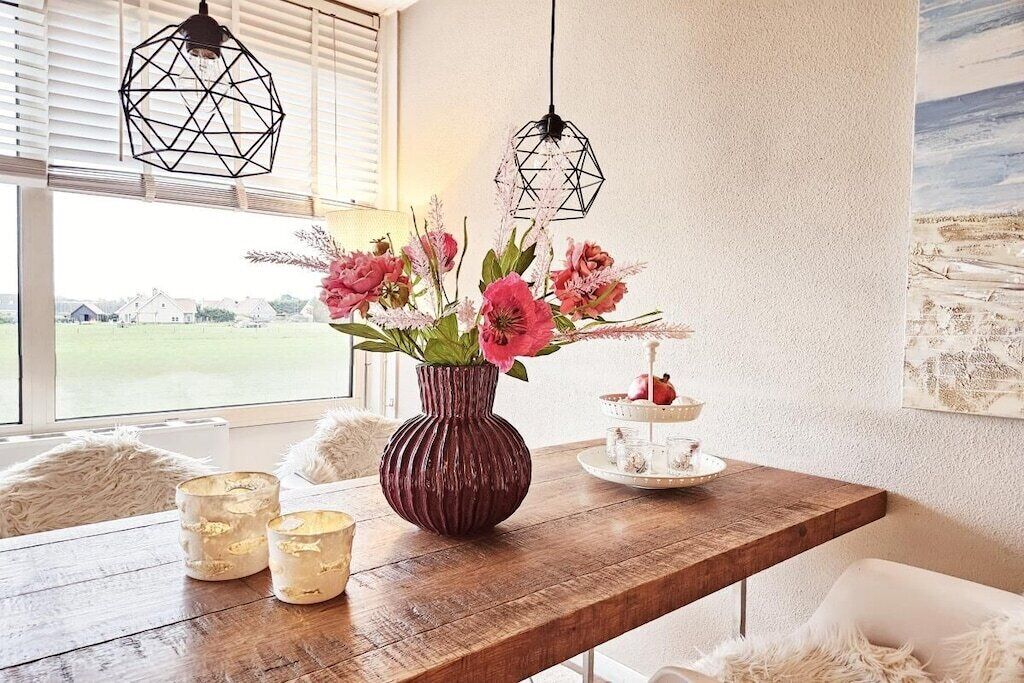 Et træbord med en vase blomster, stearinlys og et kagefad med flere etager.