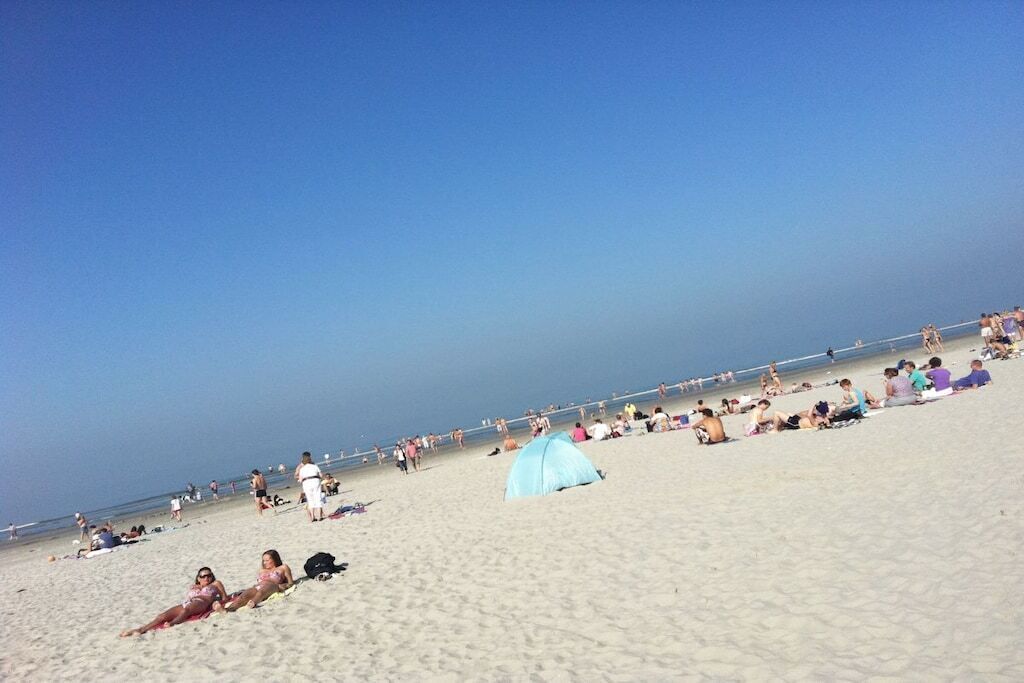 En strand med folk, der solbader og går en tur, en klar himmel og et telt i sandet.
