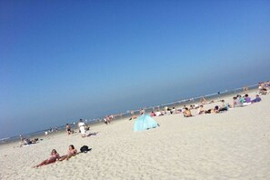 A beach with people sunbathing and walking, a clear sky, and a tent on the sand. - Amelander Paradijs 39 (KA Buren)