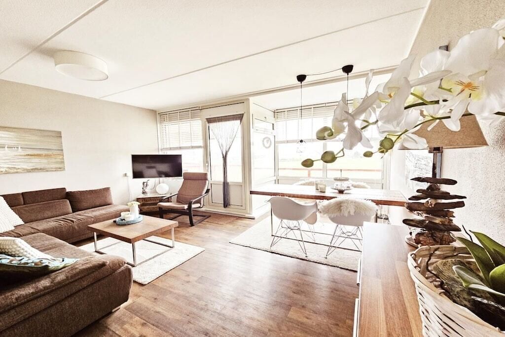 En moderne stue med sofa, sofabord og stole, et fjernsyn samt et spiseområde med bord og stole.