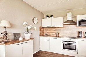 A modern kitchen with white cabinetry, a wooden countertop, a built-in oven, and a microwave. - Amelander Paradijs 39 (KA Buren)