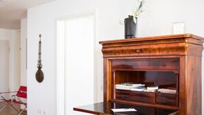 Een houten bureau met lades en een plank, een vaas met bloemen, en een rode stoel op de achtergrond.