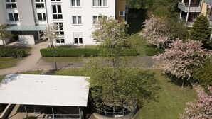 Een meerhoog gebouw met een plat dak, omringd door keurig onderhouden gazons en bomen met roze bloemen.