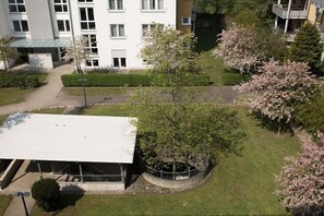 Ein mehrstöckiges Gebäude mit flachem Dach, umgeben von gepflegten Rasenflächen und Bäumen mit rosa Blüten.