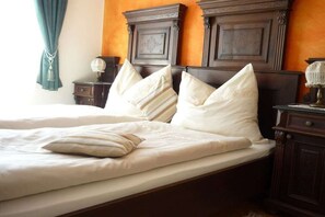 Uma cama de casal com roupa de cama branca e almofadas decorativas, uma cabeceira de madeira e uma mesa de cabeceira com abajur.