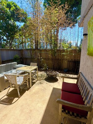 Un patio al aire libre con mobiliario de mimbre, un banco con cojín rojo y una mesa.