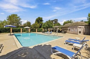 Ein Swimmingpool mit Liegestühlen und Sonnenschirmen, umgeben von Bäumen und einem Gebäude.