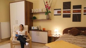 Ein Zimmer mit einem Bett, einem Sessel, einem Schrank und einer Wand mit einem 'HOME'-Schild und Kunstwerken.