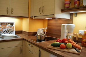 A kitchen with wooden cabinets, a coffee maker, a kettle, and fresh vegetables on the counter. - House Renate for Singles (Schönau am Königssee)