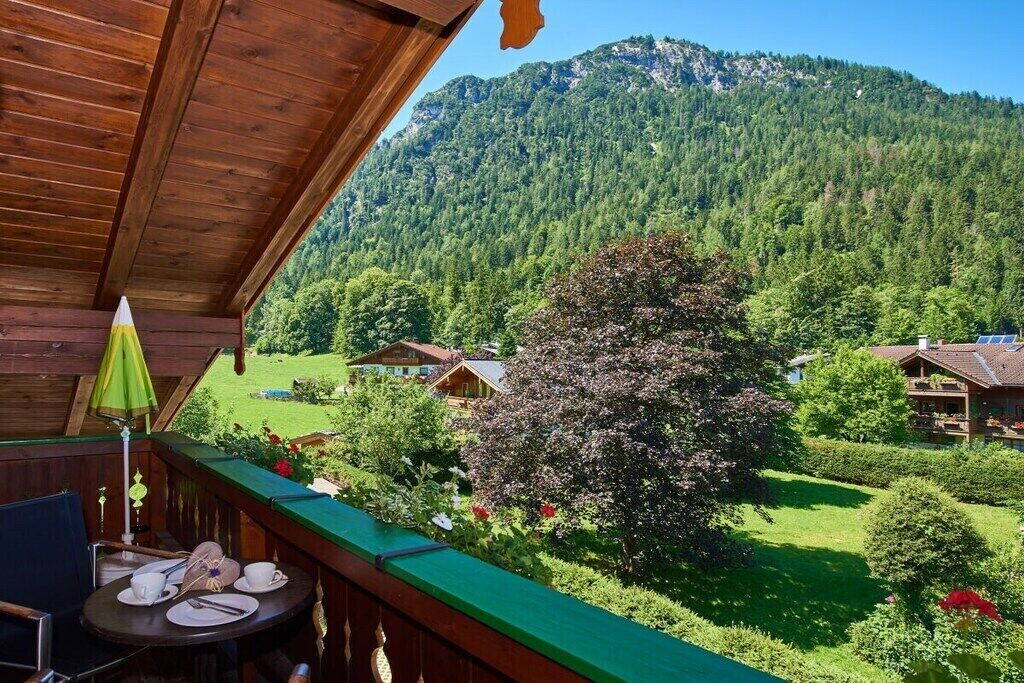 A wooden balcony with a table set for dining, overlooking a lush green landscape and a mountain.