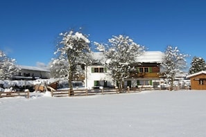 A snow-covered landscape with a building that has multiple windows and a wooden fence. - Grünstein in the Thiele House (Schönau am Königssee)