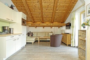 A kitchen with white cabinets, a wooden ceiling, a sofa, a coffee table, and a trash bin. - Grünstein in the Thiele House (Schönau am Königssee)
