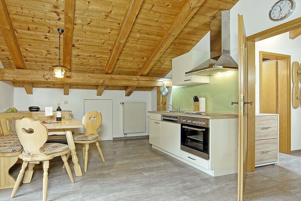 Eine Küche mit Holzbalken, einem Esstisch mit Stühlen und einer Uhr an der Wand.