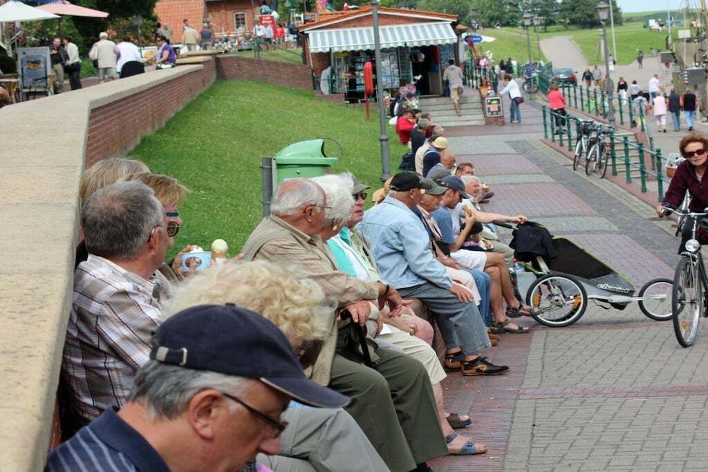 Eine Gruppe von Personen sitzt auf einer Backsteinmauer, einem gepflasterten Weg und einem Fahrrad.