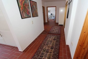 Ein Korridor mit gemusterten Teppichen, einer Holztür und zwei gerahmten Kunstwerken an der Wand.