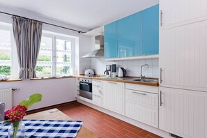 Cuina amb armaris blancs, tauleig blau i finestra amb cortines.