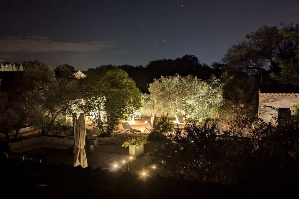 Ein Außenbereich bei Nacht mit Pool, Liegestühlen und stimmungsvoller Beleuchtung.