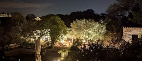 Ein Außenbereich bei Nacht mit Pool, Liegestühlen und stimmungsvoller Beleuchtung.